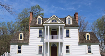 Image Of A Three-story White House With Yellow Trim Around The Windows And A Stone Foundation.